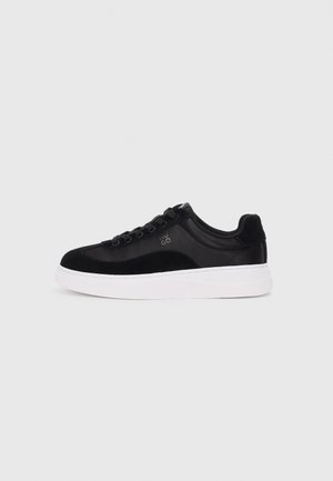 Czarny niski sneaker z czarnymi sznurowadłami, białą grubą podeszwą i małym logo "HUGO" z boku, pokazany na jasnym, jednolitym tle.