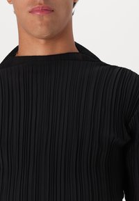 Svart plisserte skjorte med høy hals, med fine vertikale teksturer og en glatt stoffoverflate. Minimalistisk design uten detaljer.