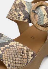 Πλατφόρμα σανδάλι με υφή πολύχρωμου μοτίβου δέρματος φιδιού. Διαθέτει στρογγυλό διακοσμητικό τοκά και σόλα σε ουδέτερο τόνο. Μέγεθος 4½.