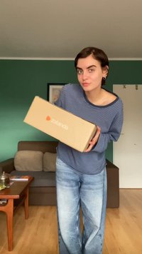 Kartónová krabica so značkou Zalando, ktorú drží osoba v modrom pruhovanom tričku a svetlomodrých džínsoch, v miestnosti so zelenými stenami.