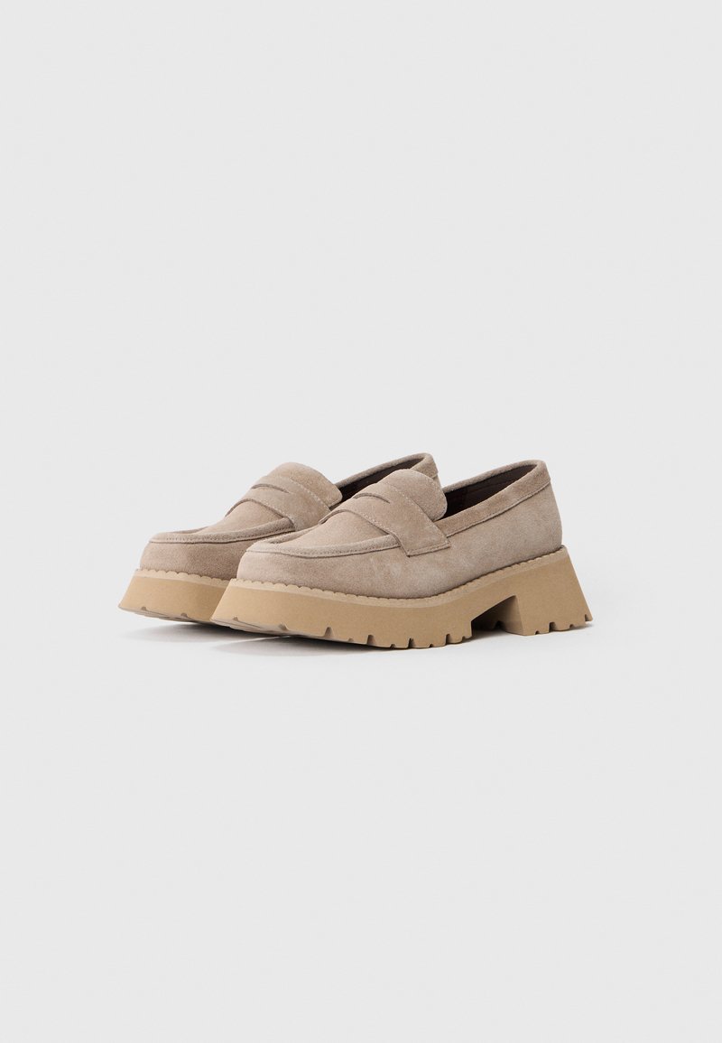 Beige Wildleder Slipper mit einer dicken, strukturierten beigen Sohle. Zu den Merkmalen gehören ein dezentes gesticktes Design auf dem Obermaterial und ein niedriger Blockabsatz.