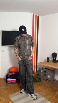 Koszulka moro z krótkim rękawem, z wzorem zielonych i brązowych liści. Luźne, ciemnoszare spodnie cargo z kieszeniami. Białe trampki.