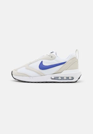 Baskets Nike blanches et beiges avec un swoosh violet, semelle à coussin d'air visible et semelle noire, vues de profil sur un fond uni.