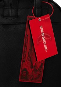 Zaino nero in tessuto testurizzato, con un'etichetta rossa con la scritta "SPRAYGROUND" e "YEAR OF THE SHARK", accompagnato da grafiche dettagliate.