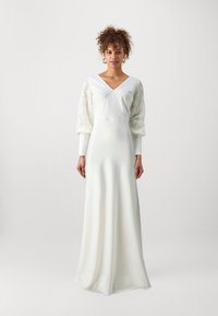 Witte lange mouw jurk met een diepe V-hals, met doorschijnende kant pofmouwen en een zachte, vloeiende stof. Eenvoudig, elegant ontwerp.