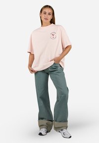 Rosa t-skjorte med korte ermer og rund hals, med grafisk trykk. Kombinert med løse, lyseblå jeans og hvite sneakers.