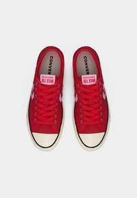 Baskets en toile rouge avec embout en caoutchouc blanc. Dotées de lacets rouges, de patchs logo Converse roses et d'un bord noir autour de la semelle. Design plat.
