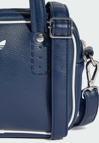 Tamnoplava teksturirana kožna torba s bijelim naglascima, s remenom od srebrnog hardvera, urezanim logotipom i prošivima.