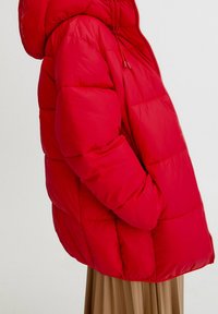 Červená péřová bunda s kapucí, s prošívaným designem a elastickými manžetami. Vyrobená z lehké, lesklé tkaniny s bočními kapsami.