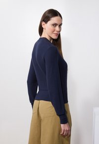 Mørkeblå strikkegenser med lange ermer og avpasset midje, parret med kaki vide bukser med baklommer og synlig søm.