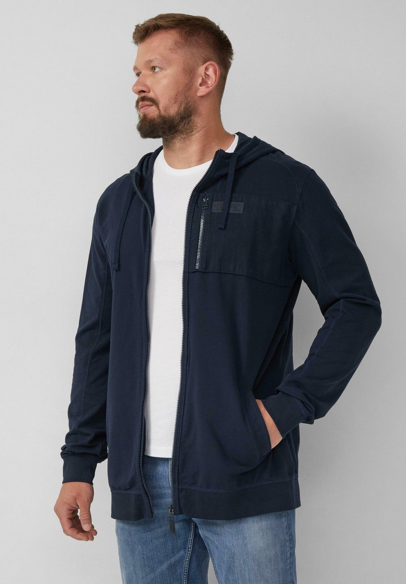Felpa con zip di colore blu navy, con un pannello frontale testurizzato, cappuccio con cordino e tasche laterali. Realizzata in tessuto morbido, presenta dettagli di cucitura a contrasto.