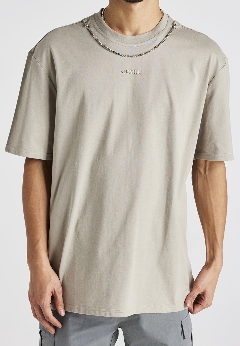 Světle béžové tričko s krátkým rukávem z bavlny, kulatým výstřihem a vyšívaným logem "SikSilk". Nosí se s platinovým řetízkem.