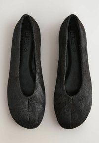 Paire de chaussures de ballet noires et plates avec une surface extérieure douce, pelucheuse, et des bouts arrondis, vues de dessus sur un fond clair.