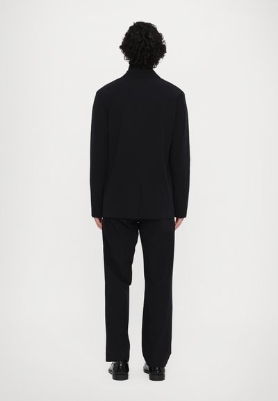 Schwarze, taillierte Anzugjacke mit hohem Kragen, kombiniert mit passenden schwarzen Hosen. Glatte Textur, figurbetontes Design und minimale Details.