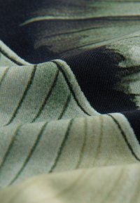 Gros plan sur un tissu doux avec des motifs abstraits de feuilles noires et vert olive et une texture tricotée visible.