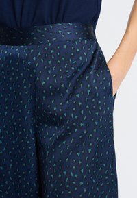 Navyblauwe broek met een satijnen afwerking heeft een teal en zwarte luipaardprint, ontworpen met zijzakken en een gladde tailleband.