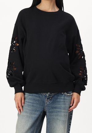 Felpa nera con inserti floreali ritagliati sulle maniche. Realizzata in un tessuto morbido, presenta un collo rotondo e un bordo a costine. Indossata con jeans sbiaditi.