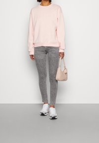 Felpa rosa chiaro con la scritta "SEOUL" in rilievo, abbinata a jeans skinny grigi, sneakers bianche e una piccola borsa rosa chiaro.