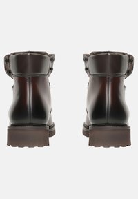 Hnědé kotníkové boty z kůže s kulatou špičkou, hladkým povrchem a dvěma dekorativními hřeby na každé straně manžety. Nízká texturovaná podrážka.