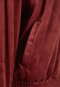 Bordeaux blødt stof med en glat tekstur, en elastisk talje og en sidelomme, der er sømløst integreret i designet.