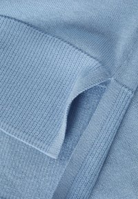 Tessuto lavorato a maglia di colore azzurro chiaro con texture variegate; presenta sezioni lisce e a coste, evidenziando cuciture e bordi sovrapposti.