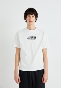 T-shirt bianco in cotone con maniche corte, caratterizzato da una stampa grafica nera che recita "29 World Cup Coupe du Monde" sulla parte anteriore.