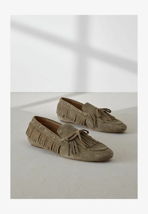 Mocassini in suede verde oliva con dettagli in frange, texture morbida e suola piatta. Presentano lacci e accessori metallici lungo i lati.