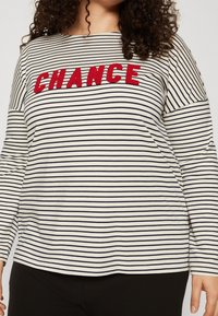 Striped long-sleeve top in cream and navy features embroidered "CHANCE" in red. Made of soft fabric with a relaxed fit and round neckline.