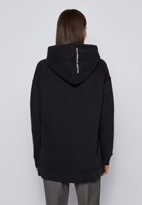 Černá mikina s kapucí, volného střihu, s klokankou, žebrovanými manžetami a logem na zadní straně. Jemná textura.