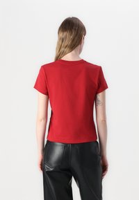Camiseta roja de manga corta hecha de algodón suave, con un cuello redondo clásico y una silueta ajustada. Se lleva con pantalones negros de imitación cuero.