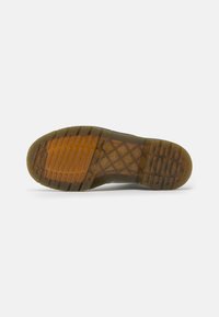 Sola de sapato de borracha com superfície texturizada; apresenta ranhuras horizontais e verticais, realces castanho claro e uma borda superior transparente.