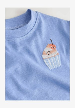 Tricou de bumbac albastru deschis, cu un design brodat de cupcake cu accente de cremă, maro și cireșe, pe un fundal de țesătură netedă.