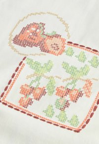 Biela tkanina so vyšívanými dizajnmi jahôd a vínneho hrozna v červenej, zelenej a oranžovej farbe, s krížikovým stehom a hnedými akcentami.