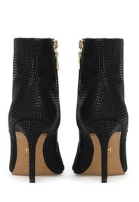 Melni augstpapēžu potīšu zābaki ar austi tekstūru, zelta rāvējslēdzēja akcentiem un stūrainu degunu uz brūnas zoles.