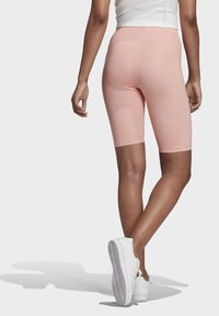 Rosa cykelshorts i knälängd med en slät yta och figurnära design. Matchas med vita sportskor som har en mönstrad sula.