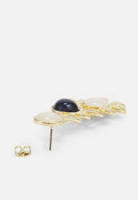 Gold-tone brooch with three oval stones: one black and two off-white. Textured leaf-like design with a straight pin and clasp.