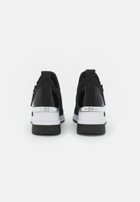 Pár černobílých tenisek s tlustými podrážkami a stříbrnými akcenty na patách, zobrazených zezadu na bílém pozadí.