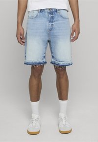 Svetlomodré džínsové šortky s rozstrapkanými okrajmi, piatimi vreckami a klasickým zapínaním na gombík. Nosené s bielymi ponožkami a teniskami.