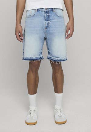 Shorts in denim azzurro chiaro con orli sfrangiati, cinque tasche e chiusura a bottone classica. Indossati con calze bianche e scarpe da ginnastica.