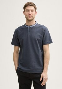 Polo shirt corto a maniche corte di un blu scuro, con un tessuto testurizzato, dotato di una patta con bottoni e un colletto di un blu chiaro a contrasto.