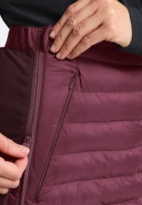 Bordeaux geïsoleerde rok met verticale quiltpatroon, voorzien van een zijzak met rits. De stof lijkt soepel en lichtgewicht te zijn.