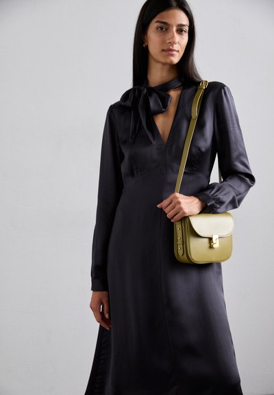 Dunkel Satin-Kleid mit langen Ärmeln und einer Schleife am Hals, kombiniert mit einer kleinen olivgrünen Ledertasche mit Umschlagverschluss.