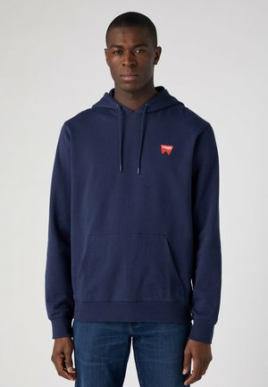 Granatowy hoodie wykonany z bawełny, z przednią kieszenią, regulowanym kapturem na sznurki oraz małą czerwoną metką na klatce piersiowej.