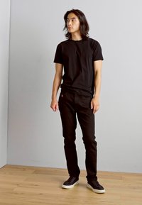 T-shirt en coton noir associé à un pantalon noir et des baskets sombres. La tenue est décontractée avec un design simple et sans motifs ni graphiques visibles.