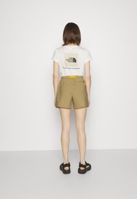 Shortsit ovat kaki-väriset ja niissä on tekstuuri-pinta. Ne sisältävät joustavan vyötärön ja sivu-ziipperitaskun. T-paita on valkoinen, ja sen takana on musta logo.