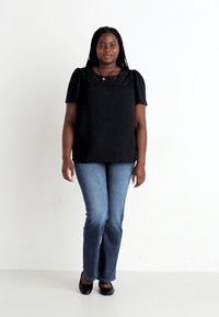 Black blouse with puff sleeves, lace neckline, paired with blue flared jeans and black flats; set against a plain white background.