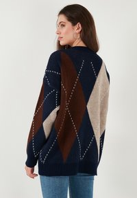 Navy, brown, and beige knitted sweater featuring a diamond pattern, ribbed cuffs and hem, oversized fit, and soft texture.