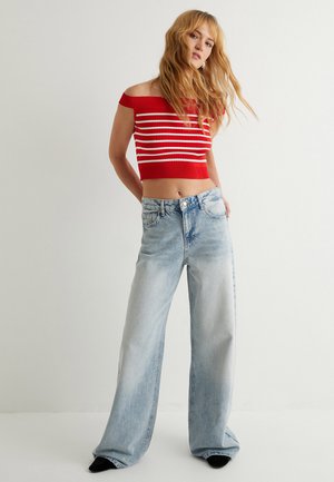 Top corto rojo con escote en los hombros y rayas blancas, combinado con jeans de pierna ancha azul claro con textura desgastada y cierre de botón.
