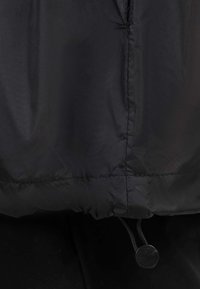 Gros plan d’un tissu noir avec une couture horizontale et un cordon avec un embout plastique rond.