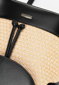 Bolso de cuero negro y paja trenzada que presenta un cuerpo texturizado, cierre superior con cordón y un acento en oro en la parte de cuero.